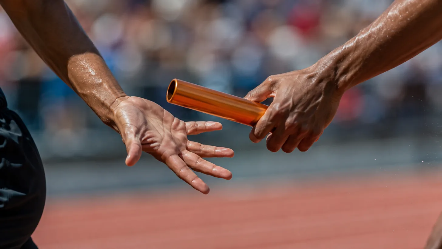 Two runners exchanging a baton mid-stride on a track.