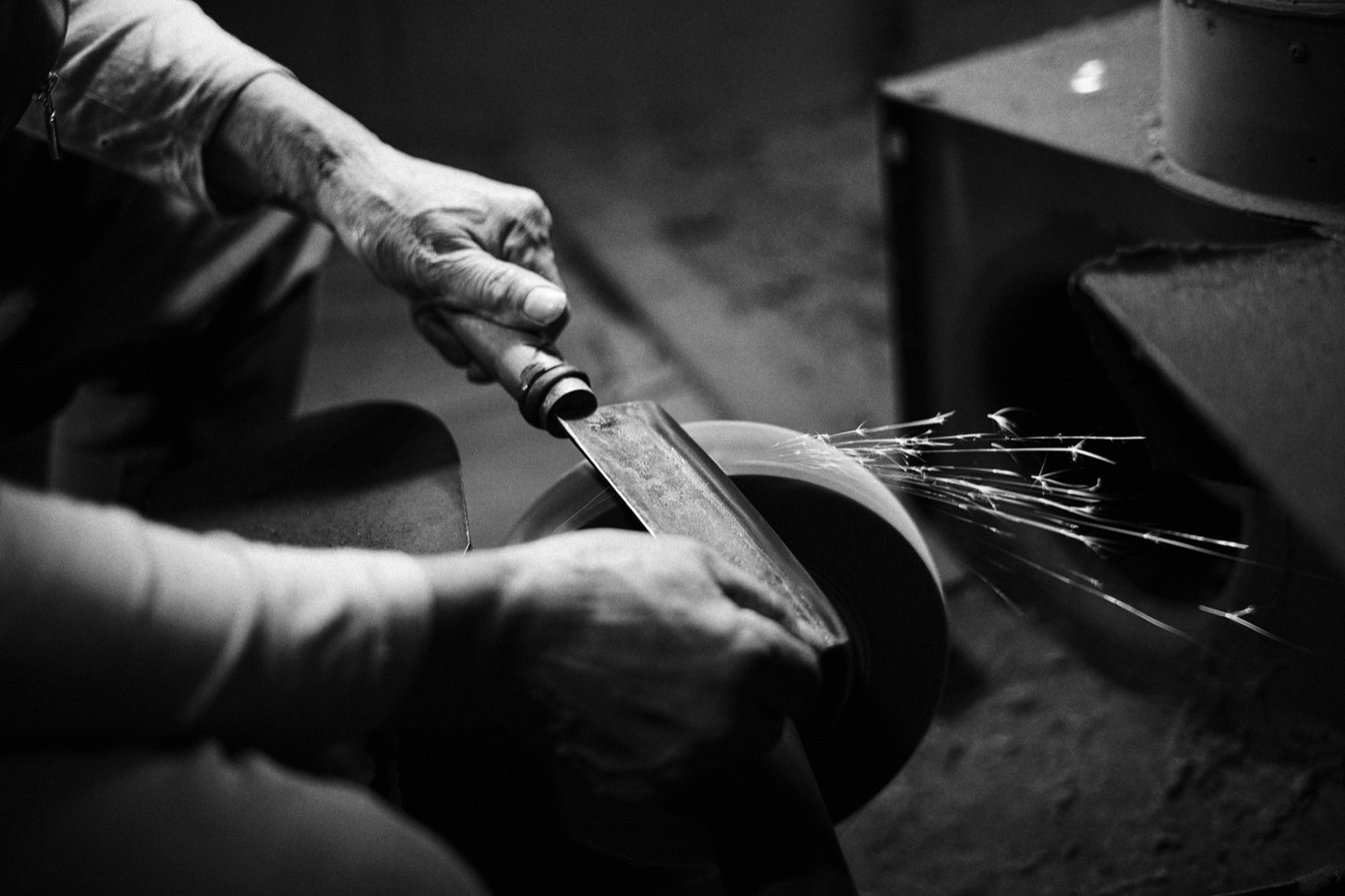 A person grinding the edge of a cleaver against a spinning wheel, throwing sparks.